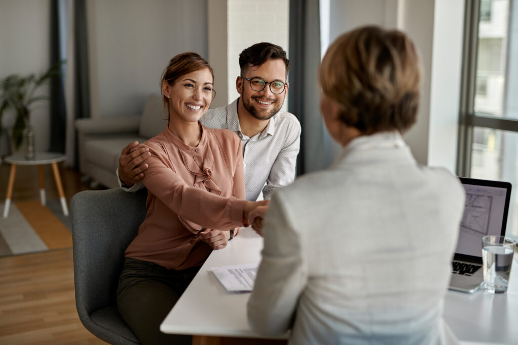 young happy couple shaking hands with insurance agent meeting office